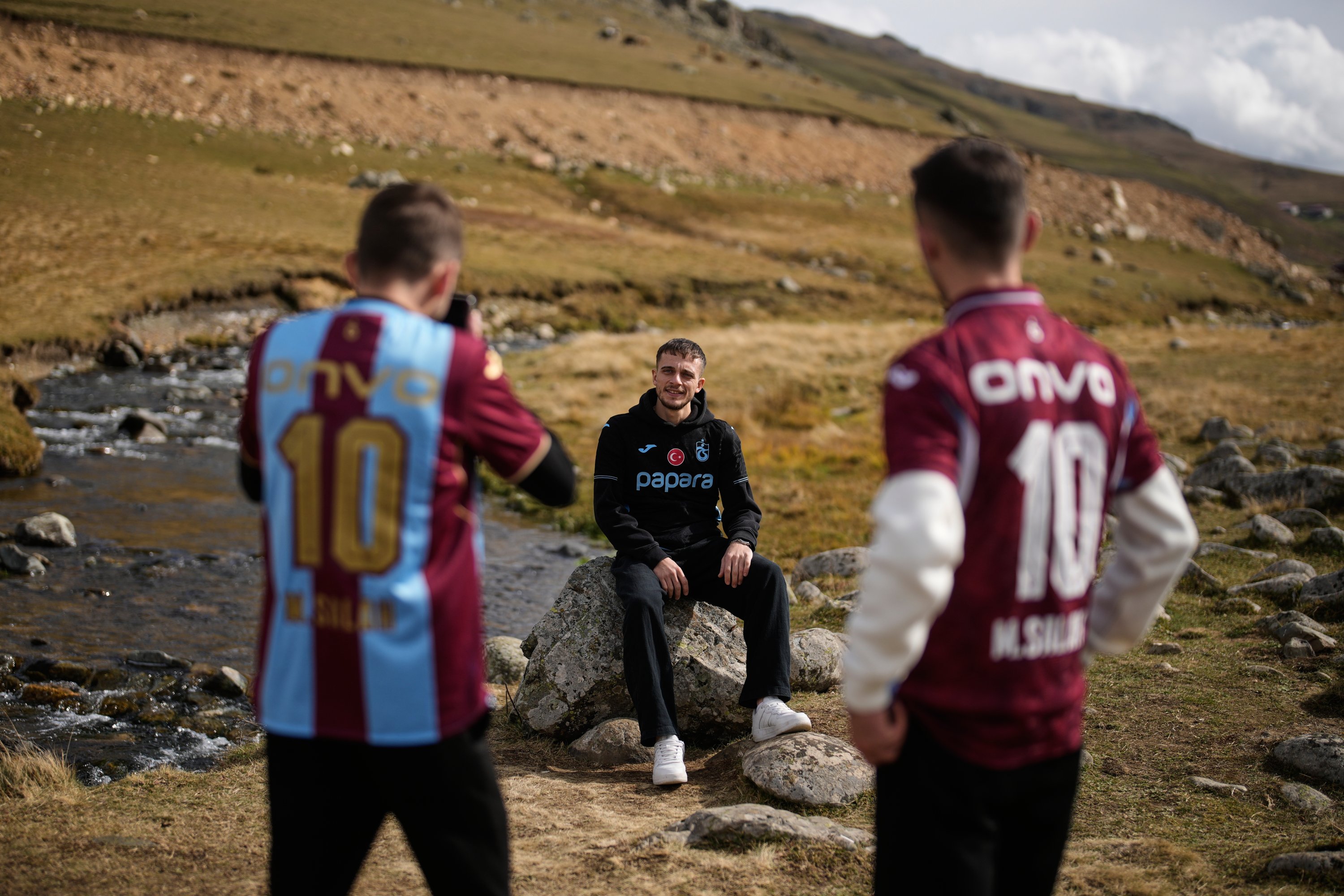 Trabzonspor fans pose for photographs on the same rock where the club's Egyptian footballer Mohamed Salah posed for a photo he later shared on social media, in Trabzon, Tükiye, Oct. 19, 2026. (AP Photo)