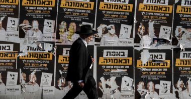 An ultra-Orthodox Jewish man walks past torn electoral posters among other posters on a wall along a street in west Jerusalem, Oct. 21, 2026. (AFP Photo)