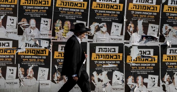 An ultra-Orthodox Jewish man walks past torn electoral posters among other posters on a wall along a street in west Jerusalem, Oct. 21, 2026. (AFP Photo)
