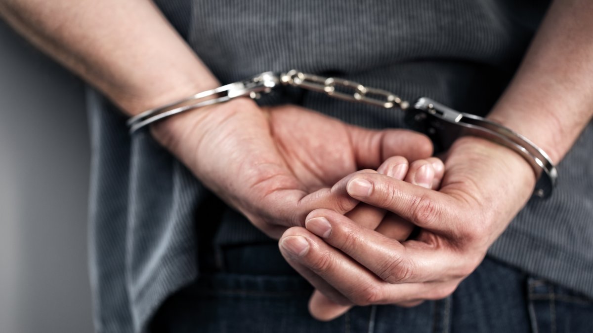 A man is arrested and handcuffed with his hands behind his back. (Shutterstock Photo)