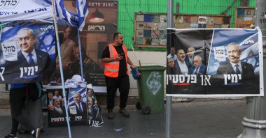 A cleaner stands next to an election poster during the country's national elections, west Jerusalem, Israel, Oct. 27, 2026. (Reuters Photo)