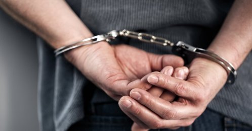 A man is arrested and handcuffed with his hands behind his back. (Shutterstock Photo)