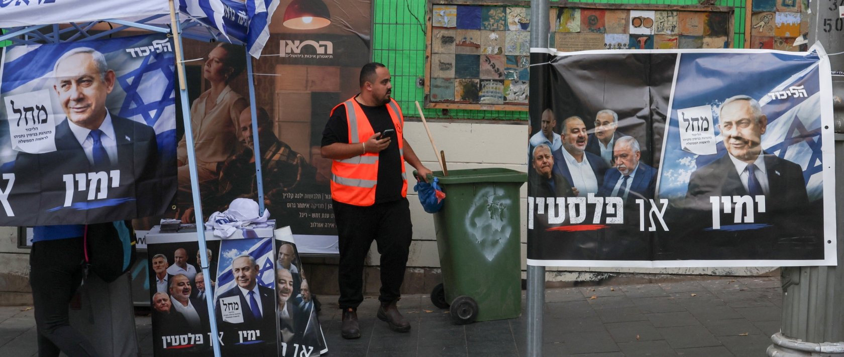 A cleaner stands next to an election poster during the country's national elections, west Jerusalem, Israel, Oct. 27, 2026. (Reuters Photo)