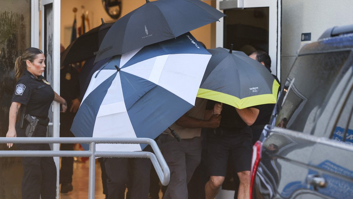 Group of people shielded by umbrellas exit the Opa Locka Executive Airport, shortly after the arrival of Flavio Bolsonaro and his family in Miami, Florida, U.S., Oct. 28, 2026. (AFP Photo)
