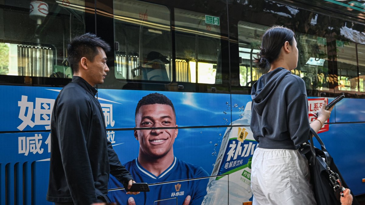 People walk past a bus featuring French football star Kylian Mbappe for Dongpeng Beverage Group's "Bushuila" electrolyte drink on a street, Shanghai, China, Oct. 27, 2026. (AFP Photo)
