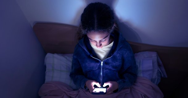 A teenager uses a smartphone in bed late at night. (Shutterstock Photo)